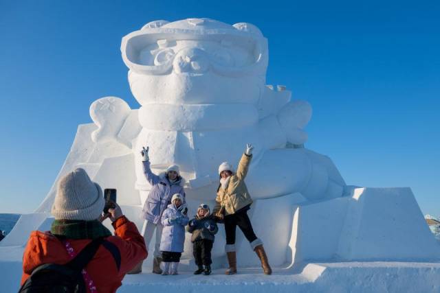 △2025年1月3日，在黑龙江哈尔滨冰雪大世界园区，游客与亚冬会吉祥物雪雕“滨滨”合影。