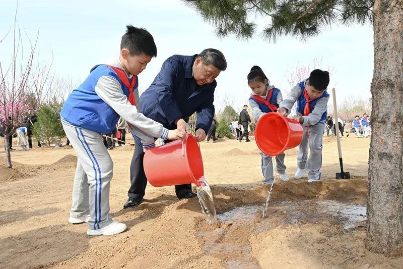 　　△4月3日，在北京市丰台区永定河畔参加首都义务植树活动时，习近平总书记同少先队员一起给刚栽下的树苗浇水。