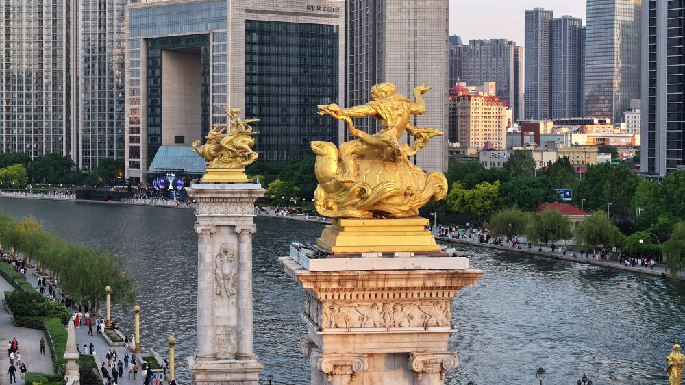 海河从天津城中蜿蜒而过,其上架设的众多桥梁链接着城市的历史与未来,也是展现天津文化海纳百川特质的一扇窗口。其中的北安桥历史最早可追溯到1939年,其设计借鉴了巴黎塞纳河上的亚历山大三世桥,桥头雕塑又吸取了中国传统文化元素。这是2024年5月1日拍摄的北安桥桥头柱及青龙、玄武雕像(无人机照片)。