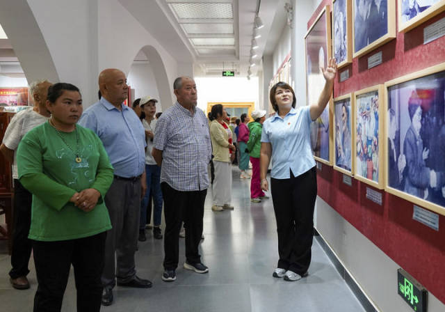 在新疆和田地区于田县库尔班·吐鲁木纪念馆，如克亚木·麦提赛地（右一）向参观者介绍展出的照片（2025年9月14日摄）。新华社记者 丁磊 摄