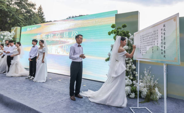2025年8月20日，在浙江省诸暨市东白湖镇斯宅村举行的集体婚礼上，新人在移风易俗倡议上签名。新华社记者 徐昱 摄