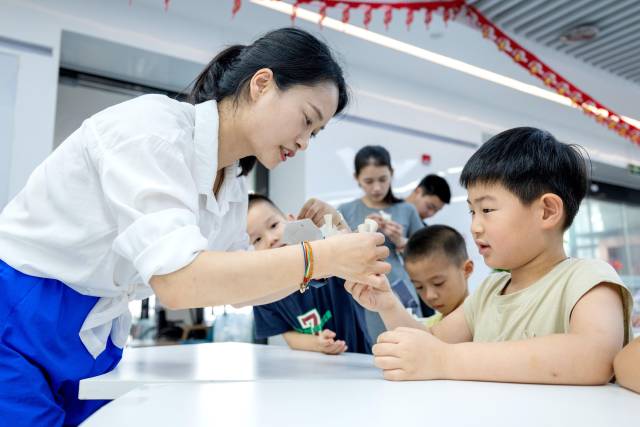 △2025年7月3日，浙江湖州长兴县龙山街道齐北社区幸福邻里中心，志愿者指导孩子们制作手工。