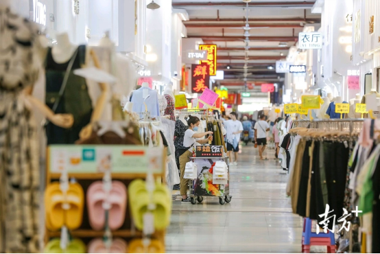 服裝城內(nèi)，人頭攢動，商鋪林立，過道兩旁擺滿了各式服飾。